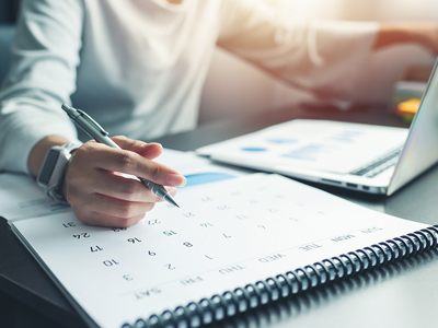 Person writing on a calendar beside a laptop