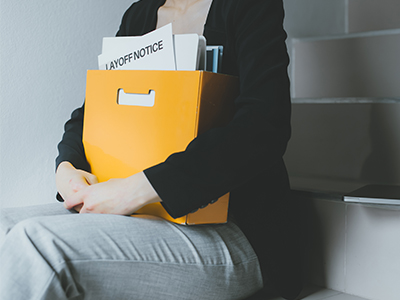 A person sitting on a flight of stairs holding their belongings in a box. A paper in the box says 