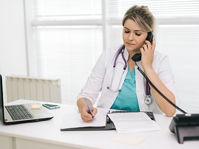 Female doctor at a desk, on the phone and writing a note