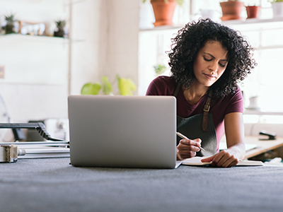 Small business woman working on laptop and writing in a journal