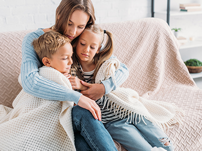 Mother on couch with her children, wrapping them in a blanket and giving them a hug.