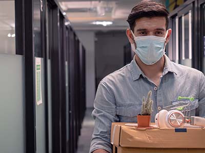 Business man wearing a mask. Leaving the office with his desk items in a box.