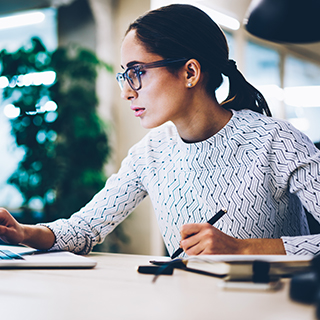 Female professional with glasses working on the computer and taking notes.