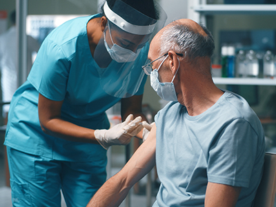 Older man being vaccinated by a nurse wearing PPE.