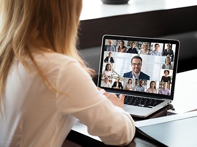 View of woman's back as she sits at a table on a video meeting.