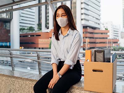 Woman wearing a mask sitting down next to a box of her desk items