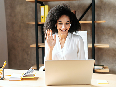 Young woman on a video call waving to person on laptop.